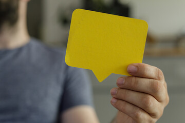 A person holds a yellow speech bubble, ideal for communication, feedback, or dialogue concepts.