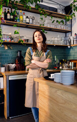 Portrait of female barista standing in her coffee shop behind the counter.