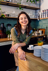 Portrait of female barista standing in her coffee shop behind the counter.