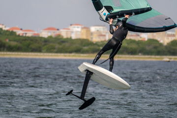 Close-up from a man in a black wet suit jumping with a wing foil at sunny weather in Netherland.