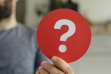 A man holds a red circle with a white question mark. Uncertainty, question, inquiry concept.