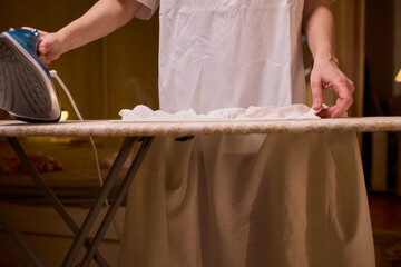 A person meticulously ironing clothes at home, ensuring all garments are neat and well cared for