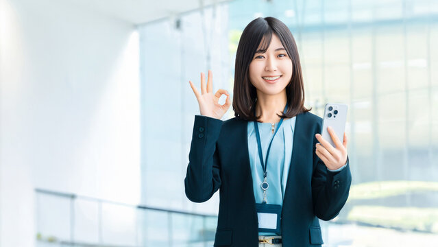 スマートフォンを持ってOKポーズをする笑顔の女性・ビジネスウーマン