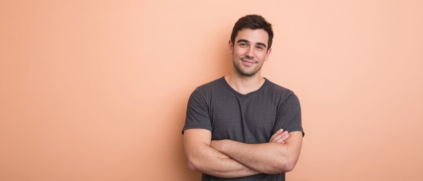 The confident young man smiles with arms crossed against a pastel wall. - Powered by Adobe