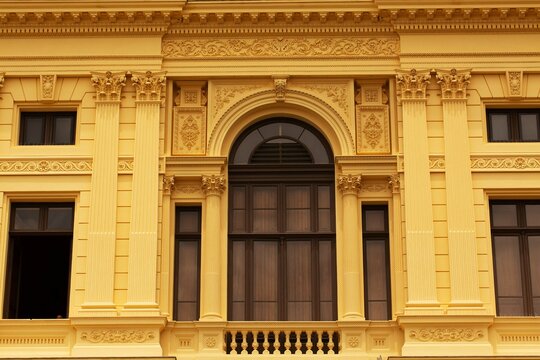 Fachada de pr&eacute;dio com constru&ccedil;&atilde;o cl&aacute;ssica, poste, c&eacute;u e pessoas passeando. 