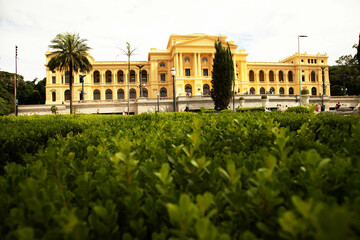 Palacete de cor amarela e jardim com muitas árvores plantas. 