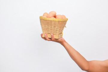 Hand Holding a Woven Basket of Brown Eggs Against a White Background