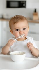 A tiny baby in a high chair carefully holds a spoon, eating porridge with focus. Softly lit, minimal kitchen emphasizes innocence, concentration, and early exploration.