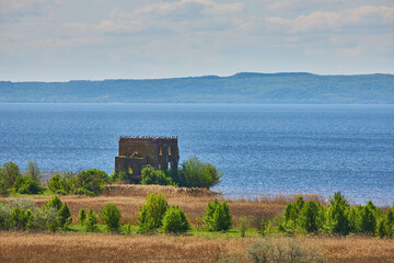 Abandoned building near a lake with birds on the roof.