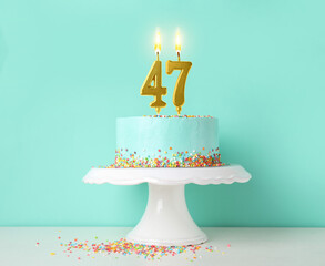 Yummy cake with burning number shaped candles and sprinkles on white table against turquoise...