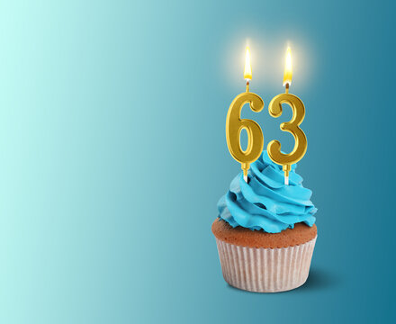 Yummy cupcake with burning number shaped candles on light blue gradient background, space for text. 63th birthday or other special occasion