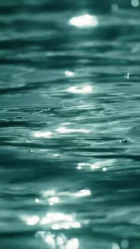 Extreme close-up macro video of a dark teal liquid surface with gentle, fluid ripples and vibrant specular highlights from low-angle direct sunlight. Very slow horizontal tracking video, tranquil and