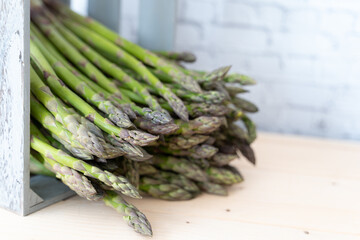 Crisp green asparagus spears falling out of a rustic gray wooden crate on a neutral background