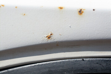 Rust on the side of a white car, close-up.