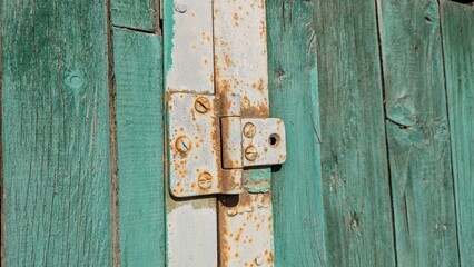 Rusty metal hinge on a teal wooden door in a rustic setting