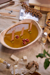 A close-up of freshly poured natural wax in a ceramic bowl with wooden wicks and dried botanicals. The process of creating an eco-friendly handmade aroma candle, combining aesthetics, craftsmanship