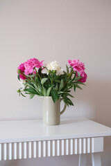 A beautifully charming arrangement of pink and white peonies in a simple vase on white vase.