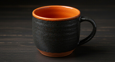 A black ceramic mug with an orange interior sits on a dark wooden surface in a studio setting
