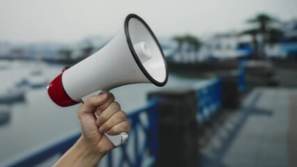 Man holding megaphone at seaside port with boats in background emphasizing communication in outdoor nautical setting.