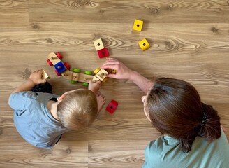 Top view of a parent and child playing with colorful wooden construction toys on a wooden floor. Early childhood development, family bonding and learning through play