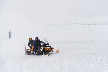 People riding a snowmobile on a snowy slope in Elbrus, Russia, with deep snow and a winter landscape
