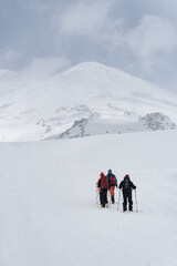 Group of climbers with backpacks and trekking poles making their way up the snowy slopes of Mount Elbrus under a dramatic cloudy sky