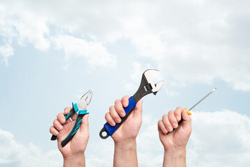 Hands of workers with different tools against blue sky with copy space