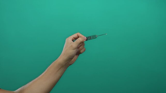 Man holding picklock tool against green isolated background, emphasizing detail, skill, and concentration.