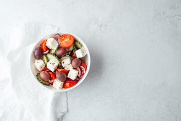 Greek salad with feta cheese olives cucumbers and tomatoes in white bowl on light background
