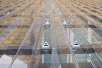 Fragment of a transparent roof made of profiled polycarbonate with fastening elements in the form...