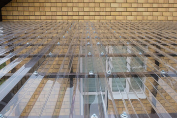 Fragment of transparent roof made of profiled polycarbonate with fastening elements in form of...