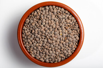Earthenware bowl full of lentils on a white background in an zenithal photograph
