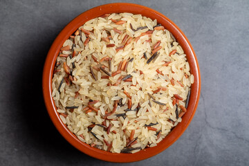 Earthenware bowl full of long, red, wild rice on a kitchen countertop in a zenithal photograph
