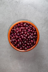 Earthenware bowl full of Anguiano red beans with a wooden spoon on a kitchen worktop in a zenithal photograph.