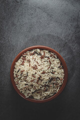 Earthenware bowl full of long, red, wild rice on a kitchen countertop in a zenithal photograph