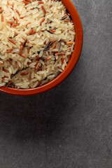 Earthenware bowl full of long, red, wild rice on a kitchen countertop in a zenithal photograph
