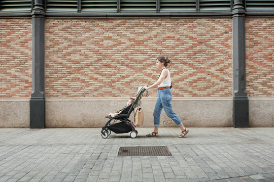 Side view of mother walking with stroller past decorative brick wall