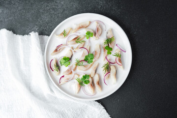 Marinated herring slices with red onion and herbs on plate with napkin on dark background