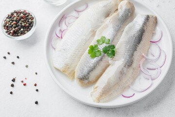 Marinated herring fillets with red onion, spices and herbs on white plate