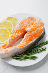 Closeup raw salmon steak with lemon slices and rosemary on plate over light background..