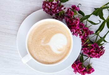 Cup of Latte with Heart-Shaped Foam and Fresh  Flowers on White Wooden Table
