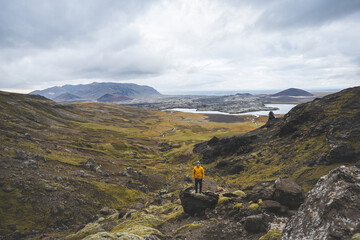 Hiker in yellow jacket stands above mossy rocks and volcanic valley on Snaefellsnes peninsula in...