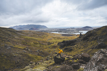 Hiker in yellow jacket stands above mossy rocks and volcanic valley on Snaefellsnes peninsula in...