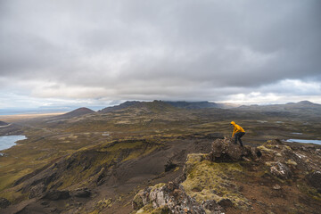 Lone hiker stands on the end of The Horn mountain on Snaefellsnes peninsula in Iceland as golden light from the setting sun illuminates the rugged volcanic terrain below. Stand on the edge