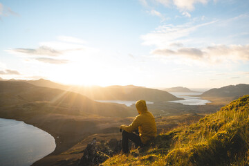 Traveler in a yellow jacket sits on the summit of The Horn on Snaefellsnes peninsula in Iceland...