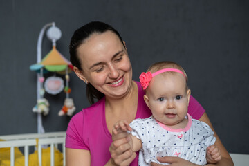 A mother plays happily with her baby girl in a cozy nursery. Warm smiles and laughter fill the room...