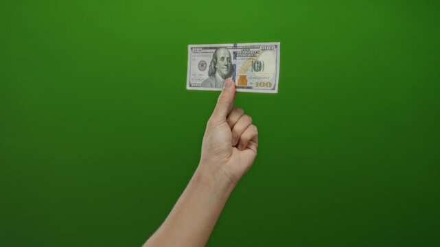 Man holds american hundred-dollar bill against vibrant green background, showcasing currency in isolated setting.