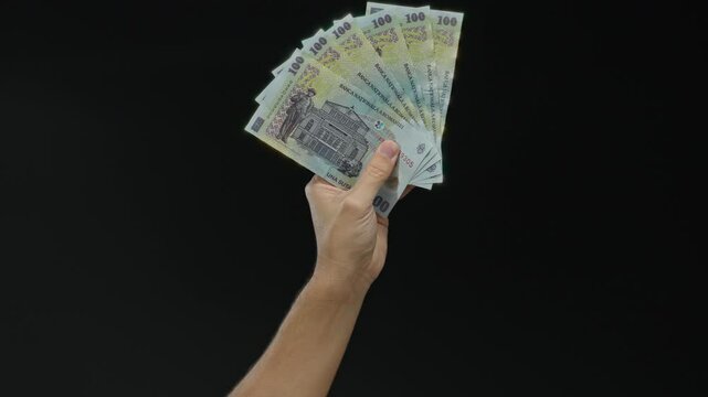Caucasian man holding romanian banknotes in hand against a black isolated background, showcasing currency, finance, business, wealth, money, banking, economy, and cash concepts.