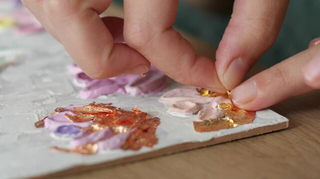 Applying Gold Leaf to Artwork: Close-up of an artist&rsquo;s hand carefully applying gold leaf to a textured painting.
