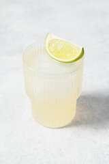 Refreshing lime cocktails on white table. Glass of citrus hard seltzer with ice cube and fresh lime...